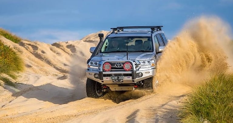 Silver Toyota Land Cruiser 200 Series off-roading through sand dunes with ARB bull bar and accessories.