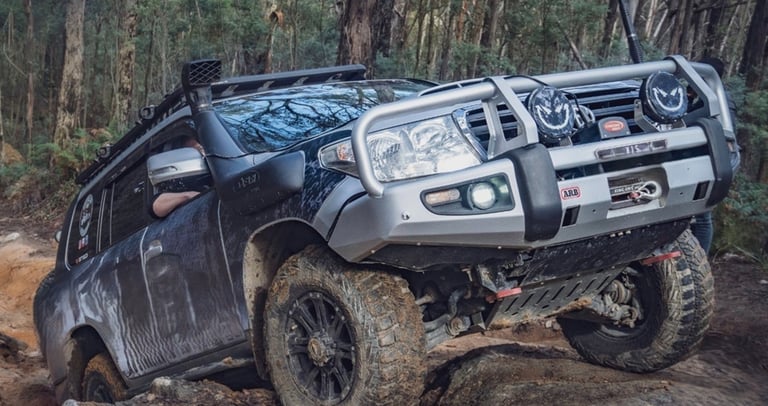 Toyota Land Cruiser 200 series 4WD with bull bar and snorkel driving over rocky terrain.