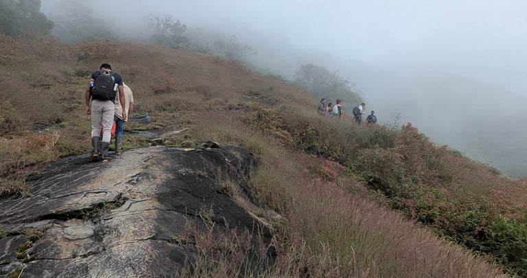 Hikers with backpacks walking along a rocky mountain ridge through thick fog and mist.