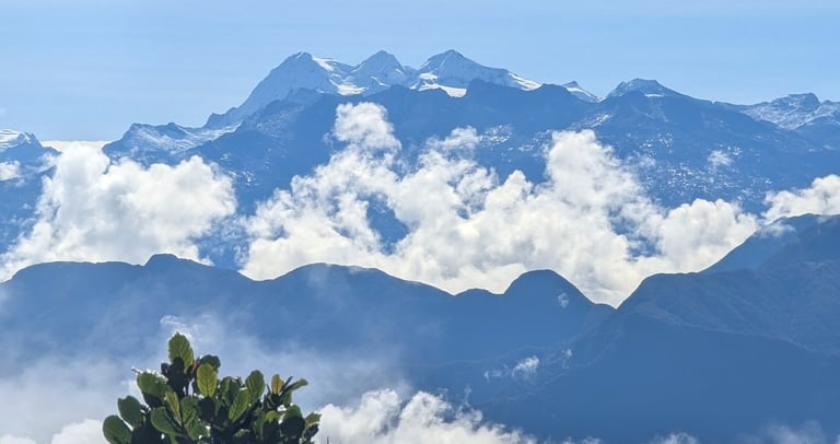 Scenic mountain range landscape with snow-capped peaks and white clouds above green trees in Minca.