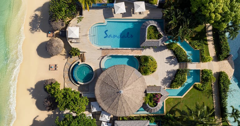 Coastal Vibe Travel - Explore Sandals Resorts a beach resort with a swimming pool and a sandy beach