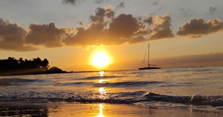 a sunset on a beach with sailboats in the background