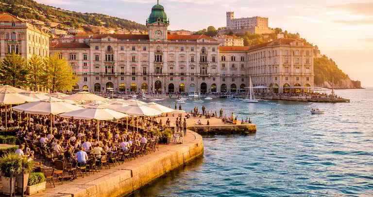 Trieste’s Piazza Unità d’Italia waterfront at golden hour, elegant historic buildings, café umbrellas, and Adriatic Sea views