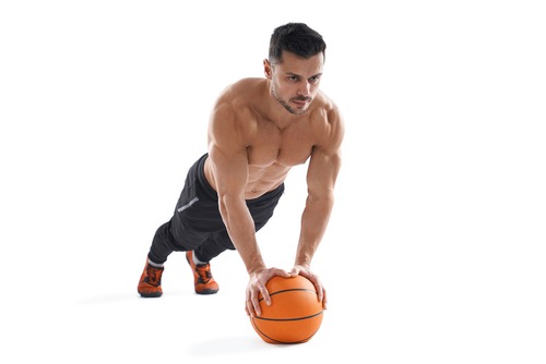 Muscular man performing a medicine ball plank for core strength and stability on a white background.