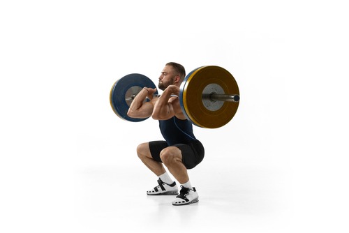 Athletic man performing a heavy front squat with a barbell for strength training on a white background.