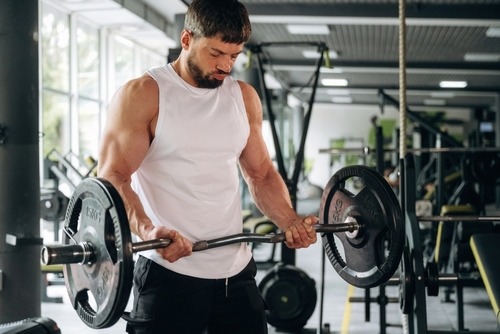 Muscular man performing bicep curls with an EZ curl barbell during a workout in a gym.