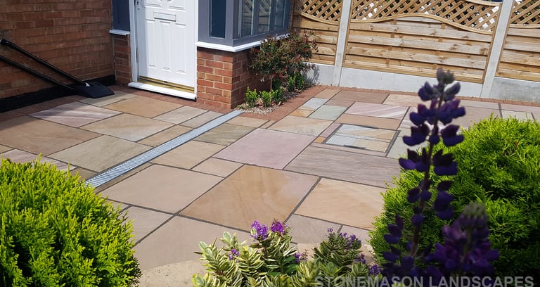 Colourful sandstone paving driveway and curved raised planter with colourful plants and flowers