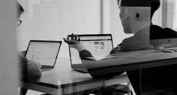 Two people with labptops talking.
