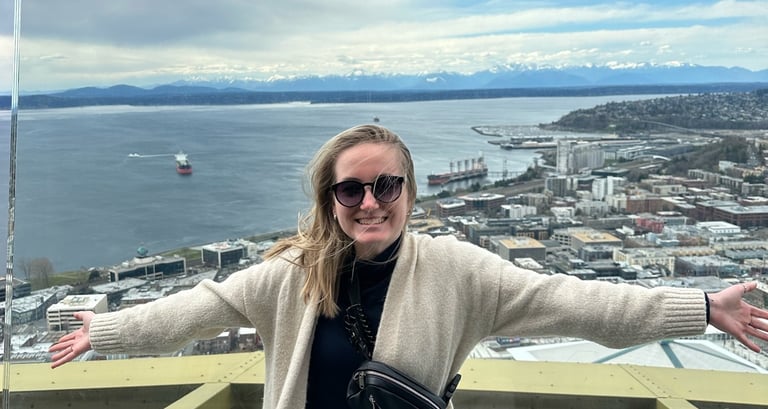 a woman on top of the space needle with the puget sound and olympics in the background