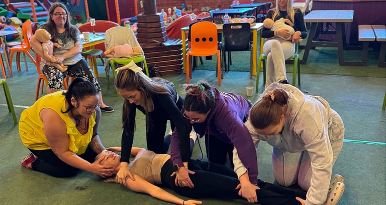 4 people kneel around a person lying on the floor during a first aid training exercise