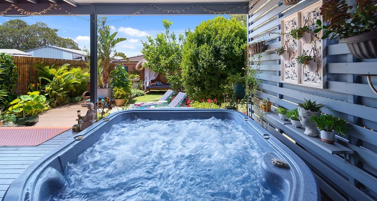 Outdoor hot tub area at Marche Home Stay with lush garden plants, cosy seating, and a relaxing covered patio.