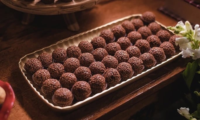 Uma bandeja cheia de brigadeiros de chocolate cuidadosamente dispostos sobre uma mesa de madeira, ce