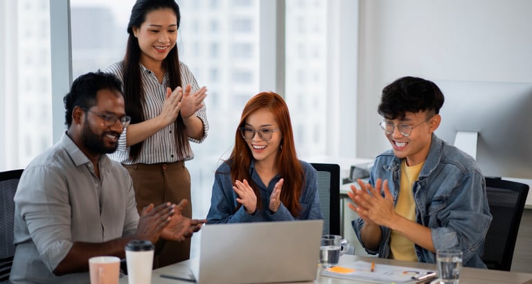Sekelompok karyawan yang tersenyum saat bekerja bersama di kantor, melambangkan kerja tim