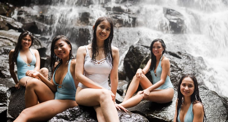 Friends sitting together on rocks near waterfall during photoshoot at Kanto Lampo Bali