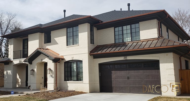 Two-story white brick home featuring copper gutters and a dark wood garage door.