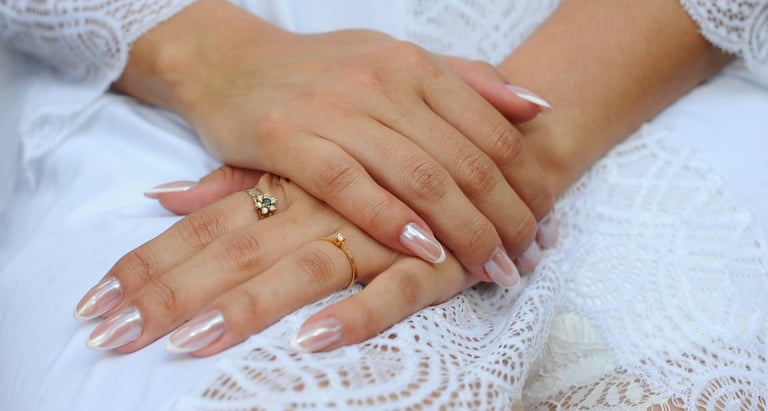 Close-up das mãos de uma noiva com manicure francesa em esmalte cromado branco e anéis de ouro,.