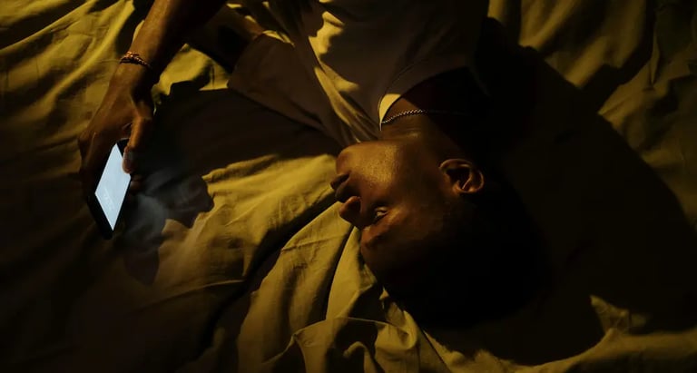 A man lying in bed at night using a glowing smartphone with blue light in a dark room.