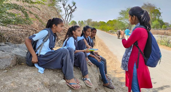 Ambassador Pooja talking to four girls seated on rock.