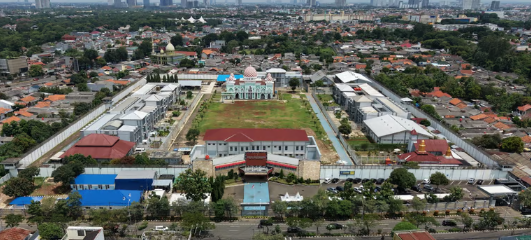 Aerial view of a walled correctional facility complex with a mosque in an urban city landscape.
