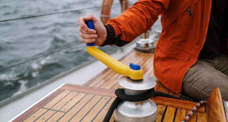 a man in a red jacket is holding a winch on a sailing boat