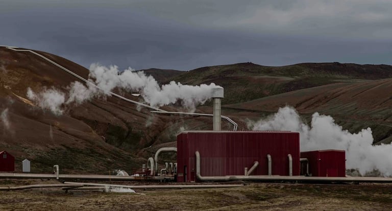 Geothermal power plant in Iceland emitting steam from a red building amidst rugged volcanic hills.