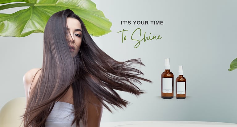 A woman with long shiny brown hair posing next to two amber glass bottles of organic hair serum.