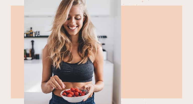 Smiling woman in fitness apparel holding a bowl of fresh raspberries and blueberries.