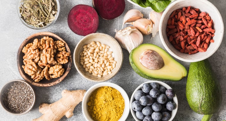 Flat lay of healthy superfoods including avocado, blueberries, walnuts, almonds, and leafy greens for a nutritious diet.