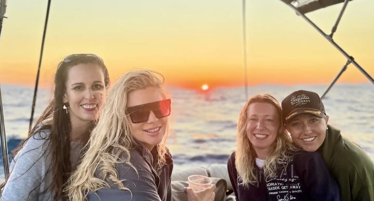 Group of female guests smiling for the camera during a sunset boat tour from Split with the Adriatic sunset in the background