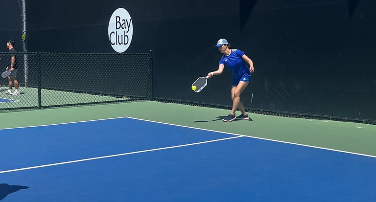 Pickleball player in blue outfit reaching for a low shot during pickleball training match.