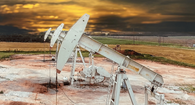 White oil pump jacks extracting petroleum in a field at sunset with a dramatic cloudy sky.