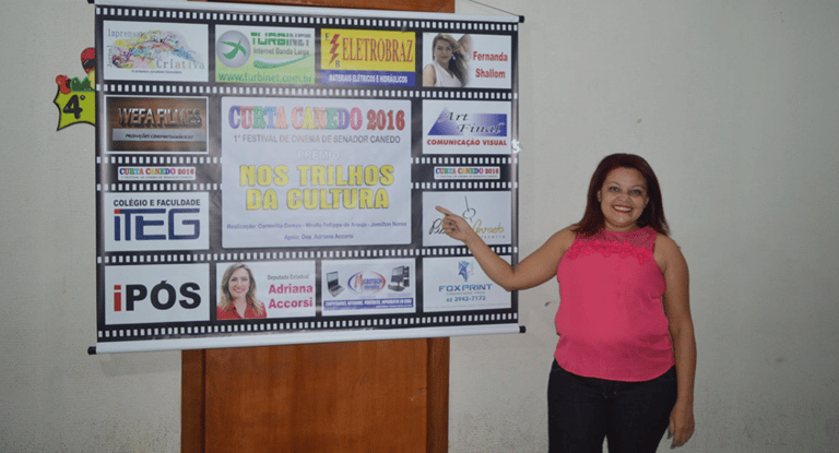 Carmelita Gomes, produtora do curta canedo aponta para o banner do curta canedo 2016