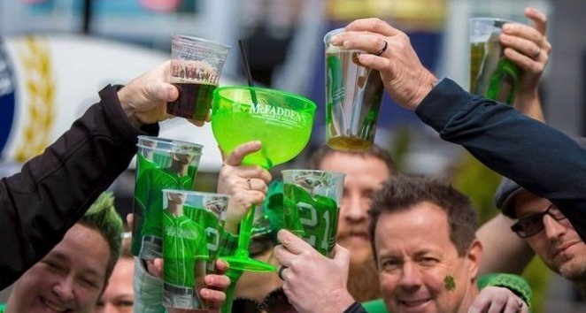 Friends celebrating St. Patrick's Day outdoors with green beer and cocktails in plastic cups.