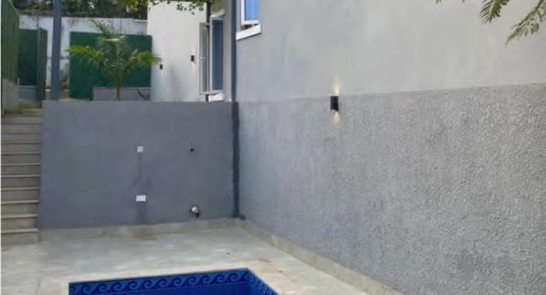 Modern outdoor swimming pool area with blue mosaic tiles and a grey textured wall.