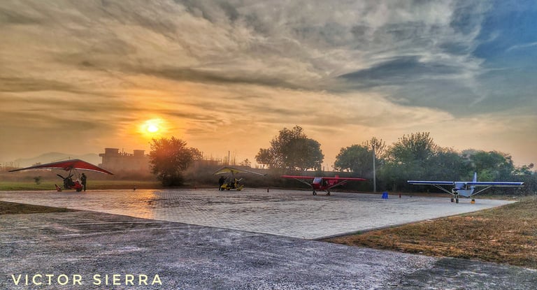 Microlight fixed wing and flexi-wing aircraft parked on the apron at sunrise during the golden hour.