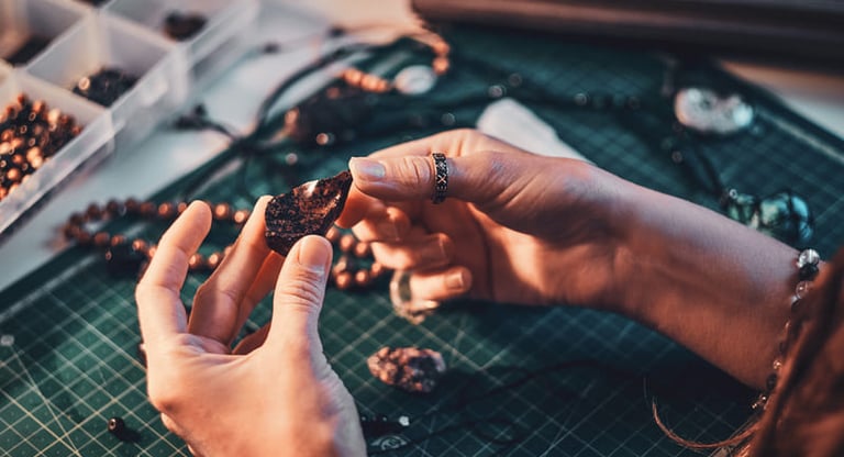 Joyero artesano inspeccionando una piedra preciosa en un banco con herramientas y materiales.