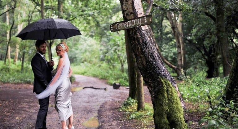 bride and groom in woodland setting holding an umbrella