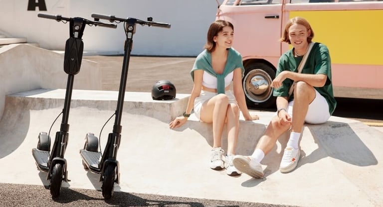 two women sitting on a skateboard in front of a van