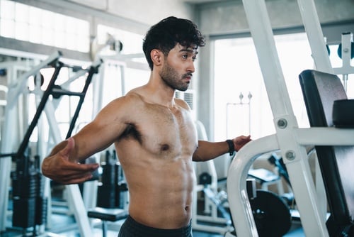 Shirtless athletic man performing chest exercises on a gym fly machine for bodybuilding.