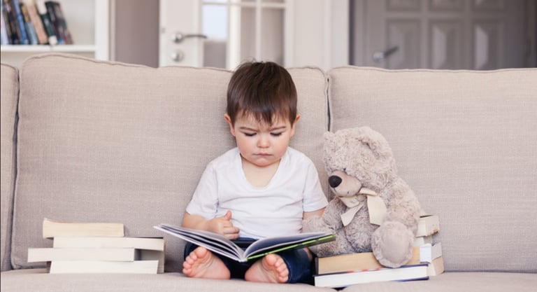 un petit garçon assis sur un canapé qui lit un livre avec un ours en peluche