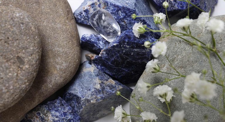 Cristales naturales de sodalita azul y piedras de río pulidas acompañadas de flores blancas