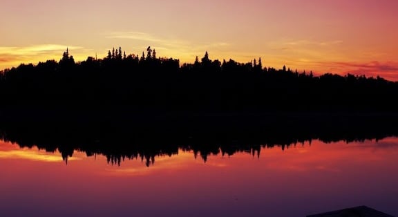 photo: reflection of fiery sunset and trees on a placid lake in Alaska