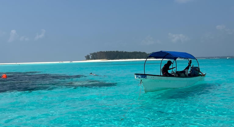 Tourists snorkeling near a boat anchored in shallow turquoise waters at Mnemba Island Zanzibar during a tropical snorkeling 