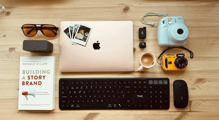 Flat lay of a workspace with a MacBook laptop, Instax camera, Trust keyboard, and Building a Storybrand book.
