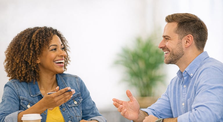 A diverse man and woman smiling and talking during a professional business meeting in a bright office