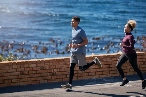 A man and woman jogging together along a scenic coastal road for outdoor fitness.