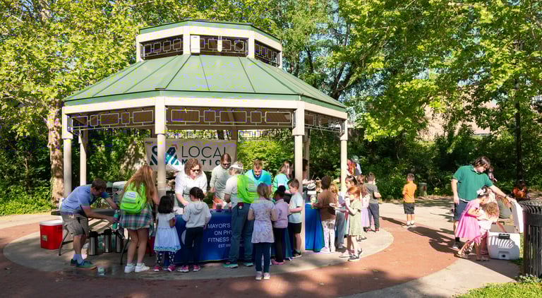 A bunch of children with a few adults approaching a table of adults in a park
