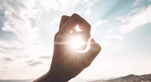 photography of sun glaring through the hole of finger