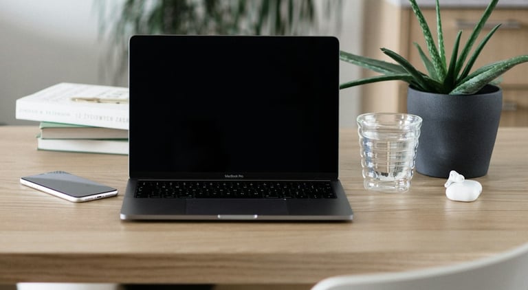 Laptop on a desk with a glass, plant and some books