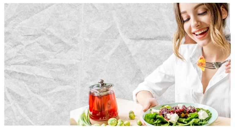 Smiling woman eating a healthy green salad with beets and cheese next to a teapot of herbal tea.